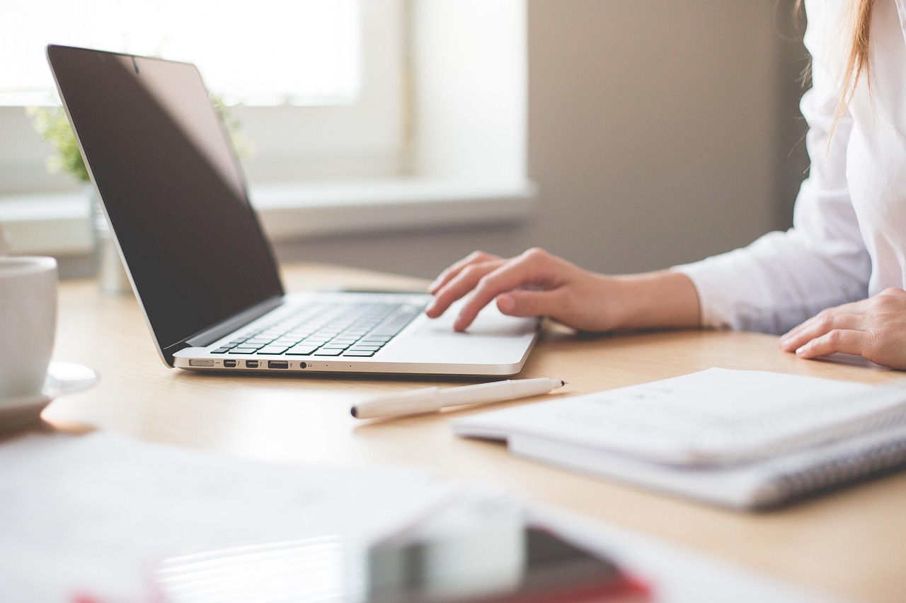 Personne travaillant sur un ordinateur portable à un bureau, avec un carnet et un stylo à proximité